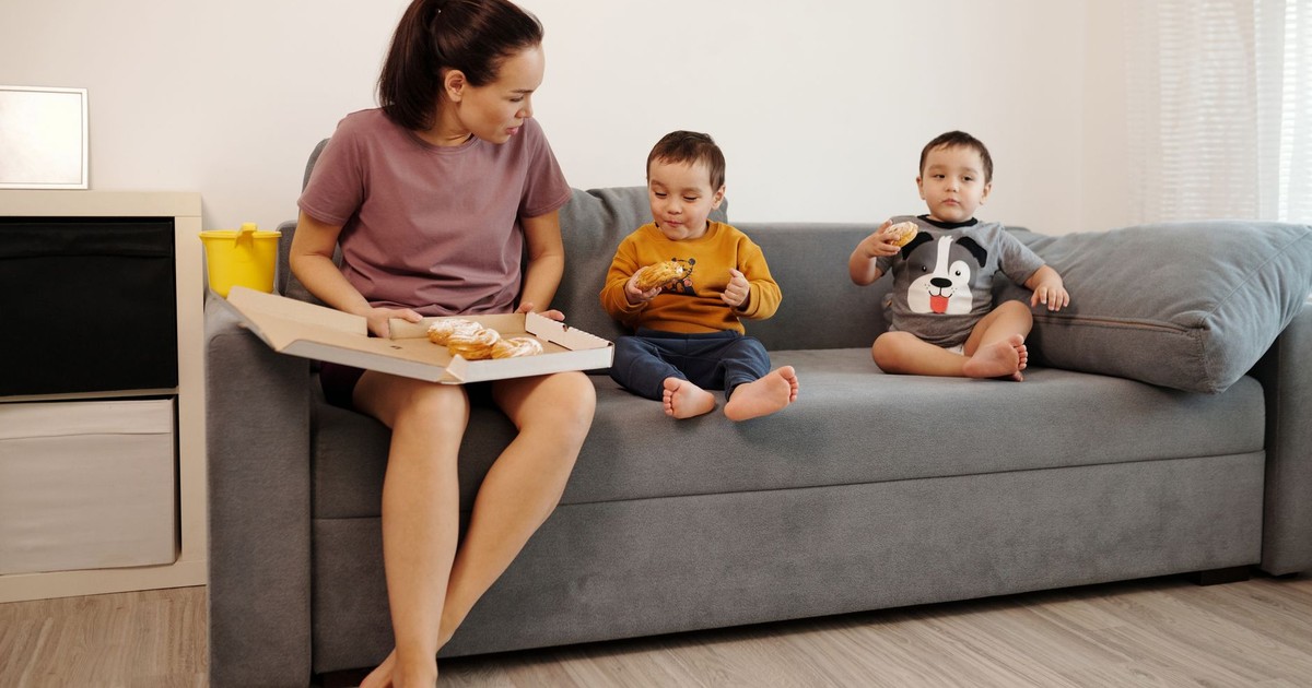 A mother and her twin toddlers enjoying croissants on a sofa, capturing a cozy family moment.