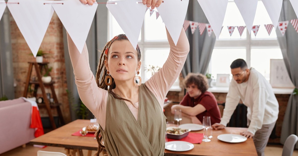 A woman decorates a dining room with bunting flags for a party gathering.