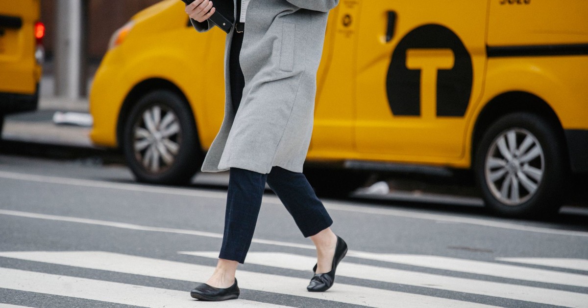 Side view crop female in formal clothes carrying documents folders crossing busy road in urban city district
