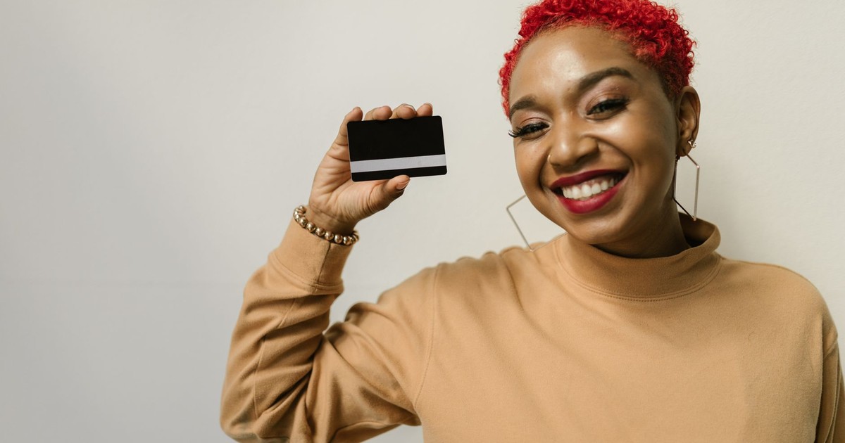 Happy woman with red hair holding a bank card, smiling against a white background.