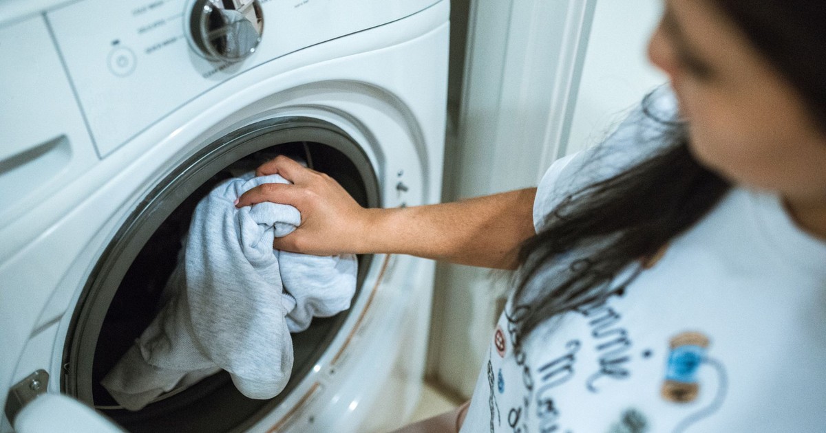 A woman loading laundry into a washing machine indoors, focusing on household chores.