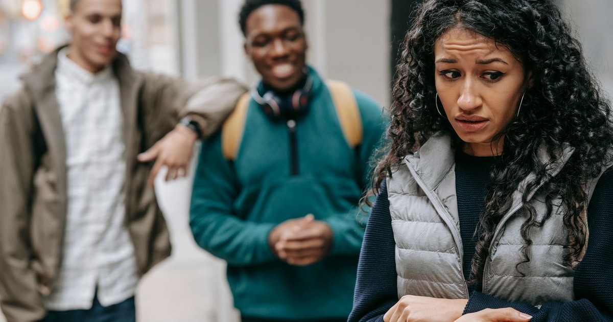 Laughing multiracial teenage boys mocking at depressed young ethnic female standing on street after school
