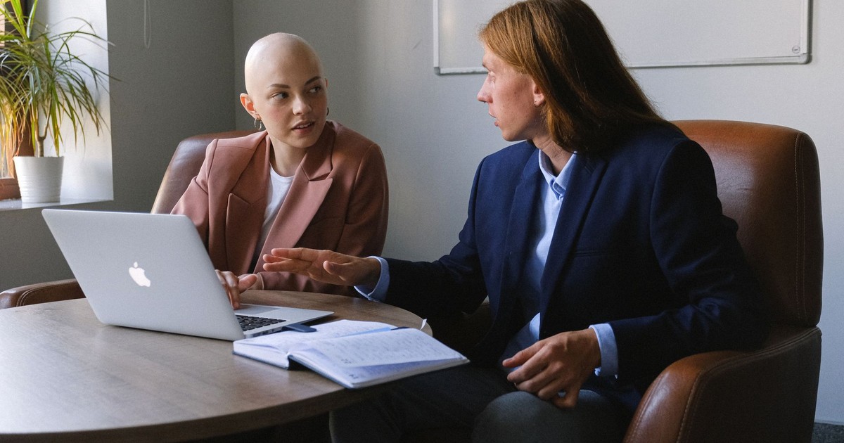 Confident young coworkers wearing formal jackets sitting in leather armchairs near table with netbook and organizer while sharing business ideas