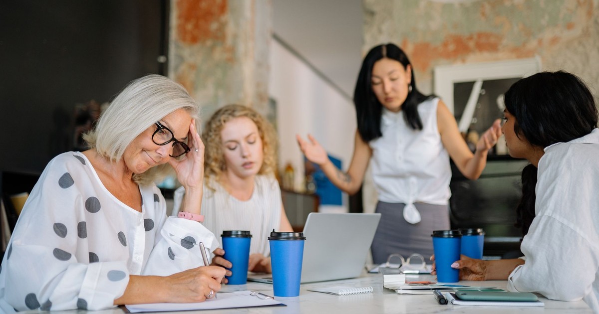 A business meeting with diverse women discussing and expressing emotions at a table.