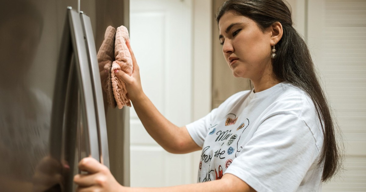 Woman cleaning a refrigerator door in a modern indoor kitchen setting with a focused expression.