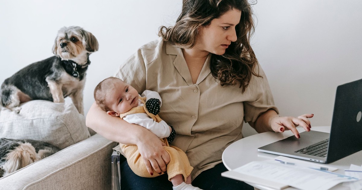 Mother balancing work from home with parenting, holding baby and typing on laptop.