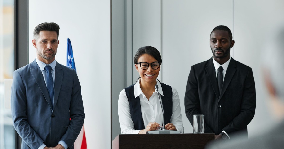 Diverse leaders at a conference podium with US flag in the background.