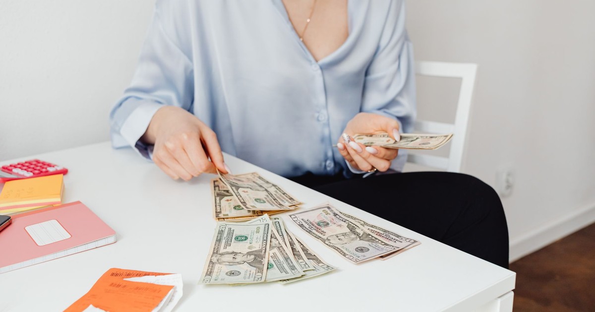 A woman counts US dollar bills at a desk, symbolizing finance management.
