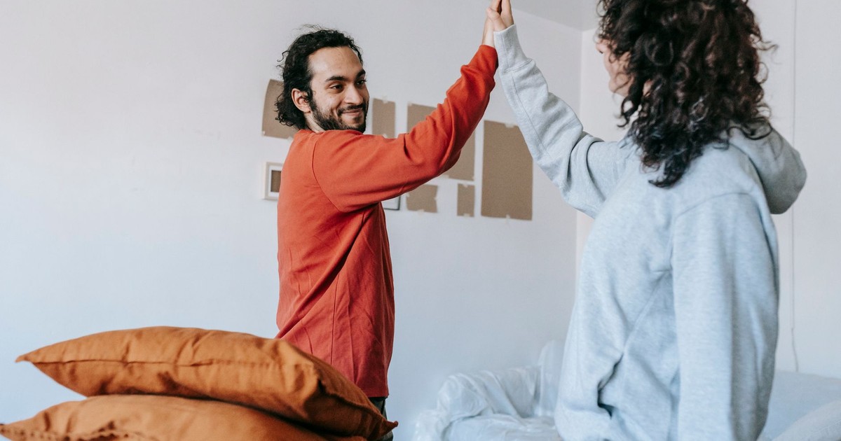 A happy couple celebrates by sharing a high five in their new home, surrounded by unpacked items.