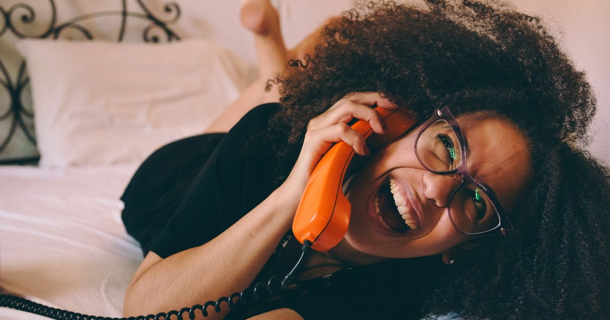Young woman enjoying a conversation on a retro orange phone while relaxing indoors.