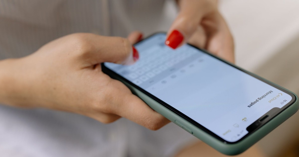 Close-up of a woman with red nails typing on a smartphone indoors, focusing on hands.