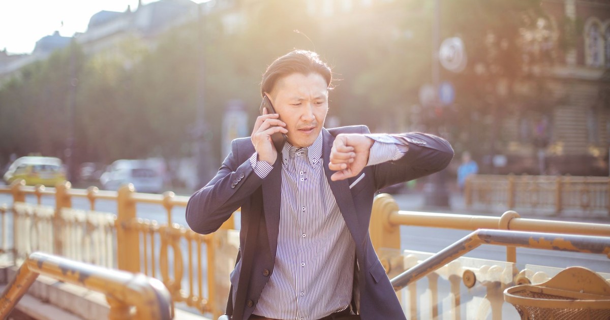 Asian businessman in suit checking time while on phone outdoors.