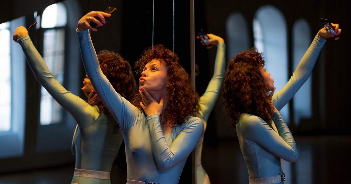 Young woman in leotard takes a selfie with reflection in a dimly lit room, showcasing a modern indoor setting.