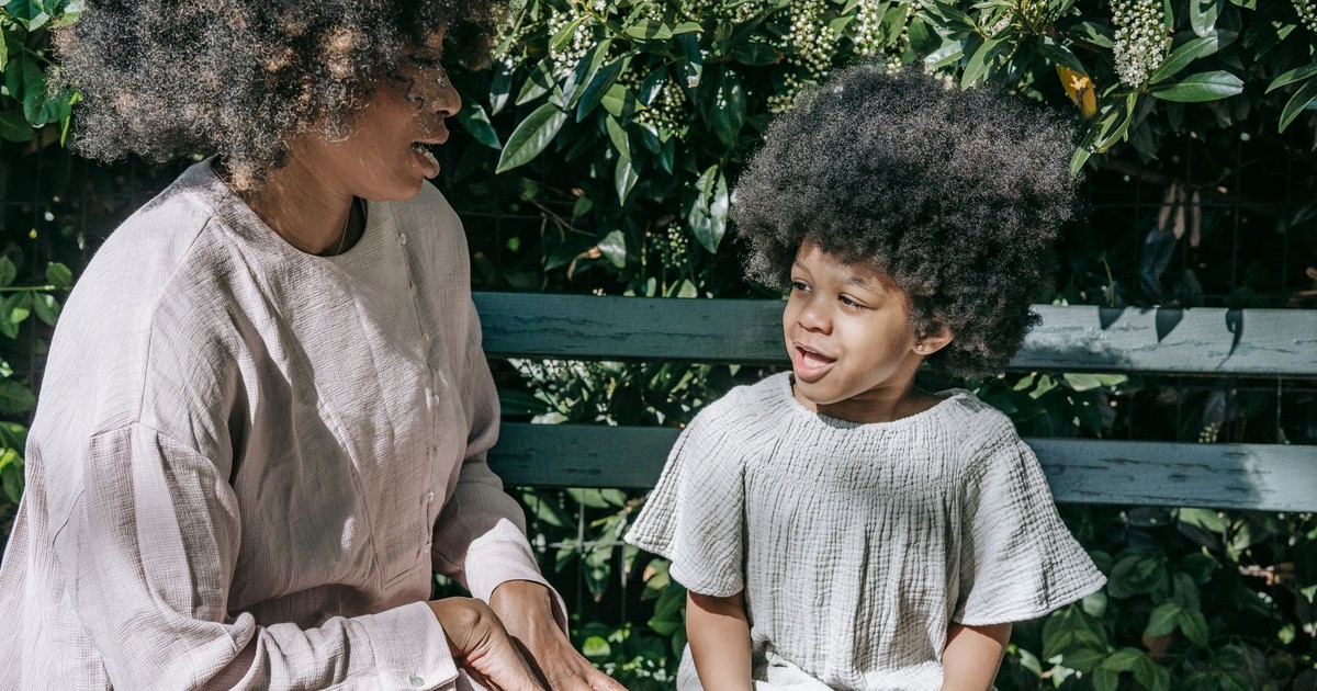 A mother and child enjoy quality time on a garden bench, surrounded by lush greenery.