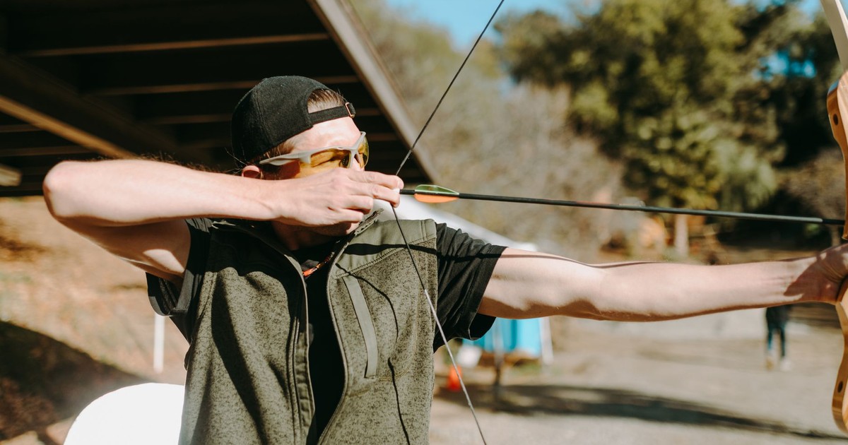 A man aiming a bow and arrow in an outdoor archery range, focusing on the target.