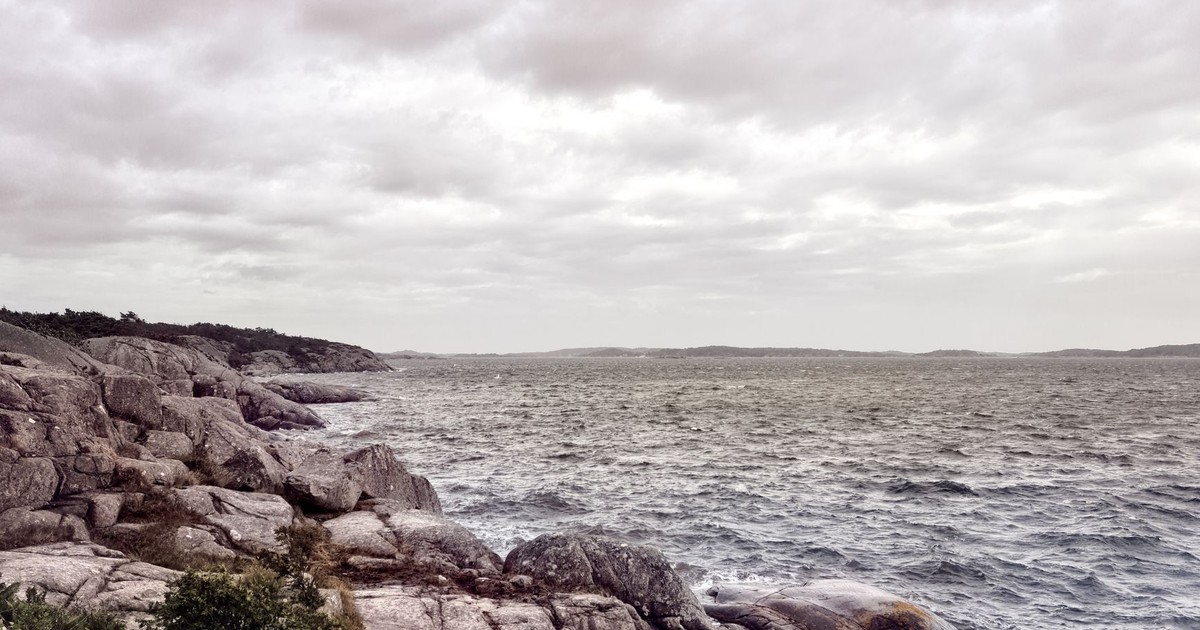 Dramatic ocean waves crash against the rocky Älvsborg coast in Sweden under a cloudy sky.