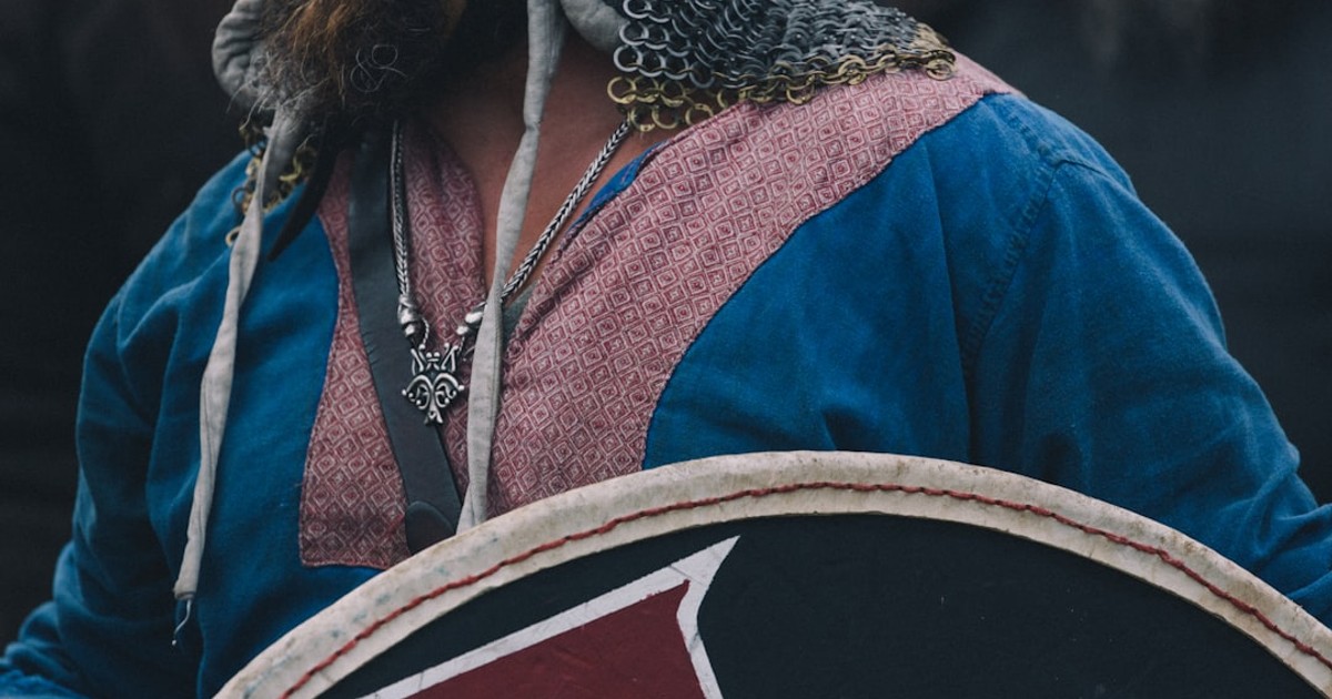 A viking warrior in chainmail and tunic holding a shield.