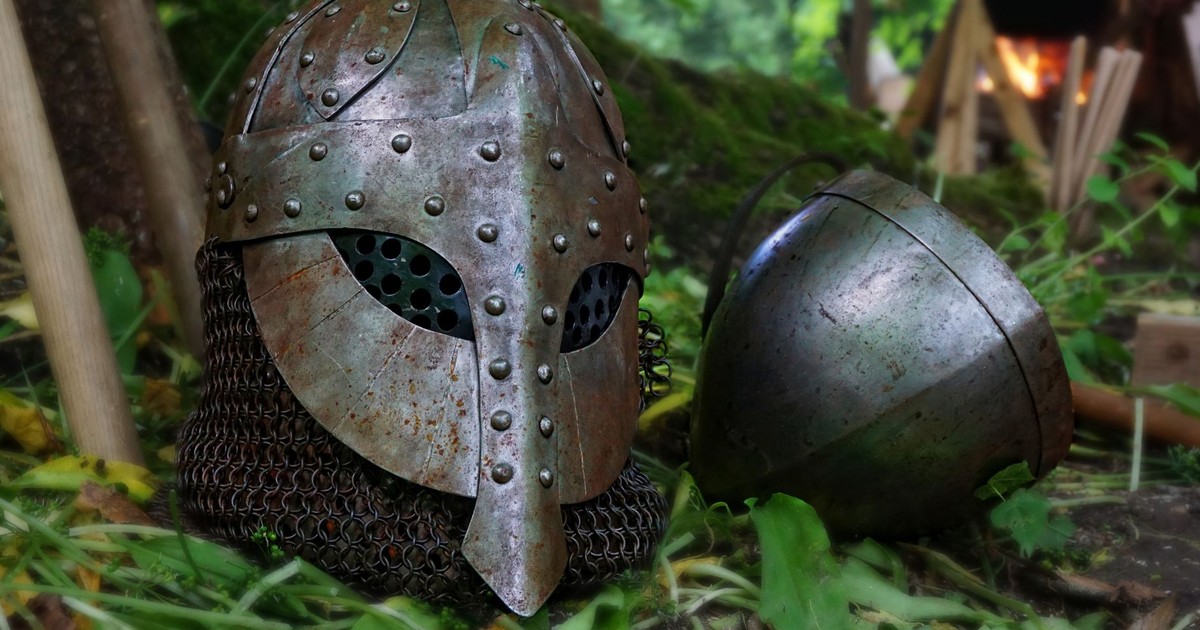 Close-up of a medieval helmet with chainmail on a forest floor, surrounded by leaves and natural elements.