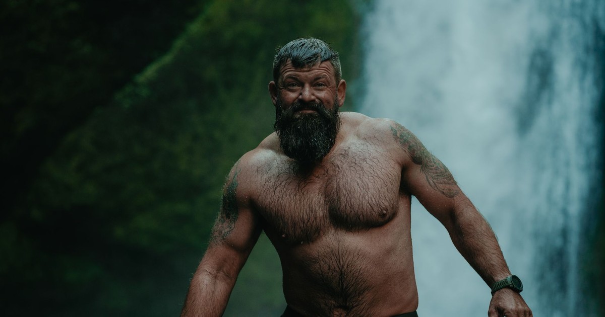 A bearded man stands shirtless in front of a waterfall in Cascade Locks, Oregon.