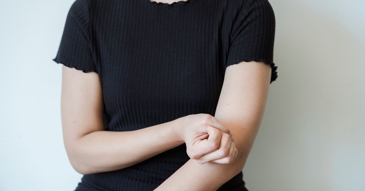 A close-up view of a woman in a black shirt holding her arm, showcasing skin contact and emotion.