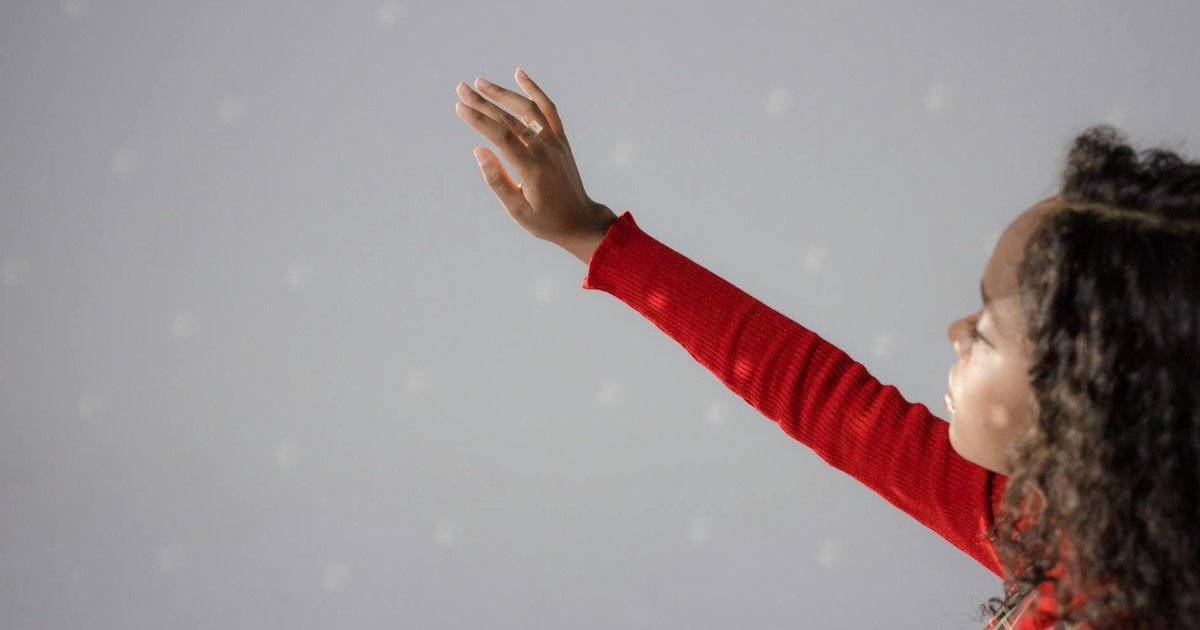 A woman in a red sweater raises her hand against a soft grey background with subtle dots, featuring copy space.