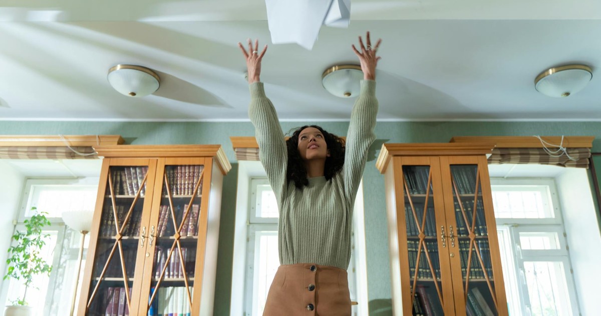 A young woman throws papers in the air in a library, expressing joy and relief.