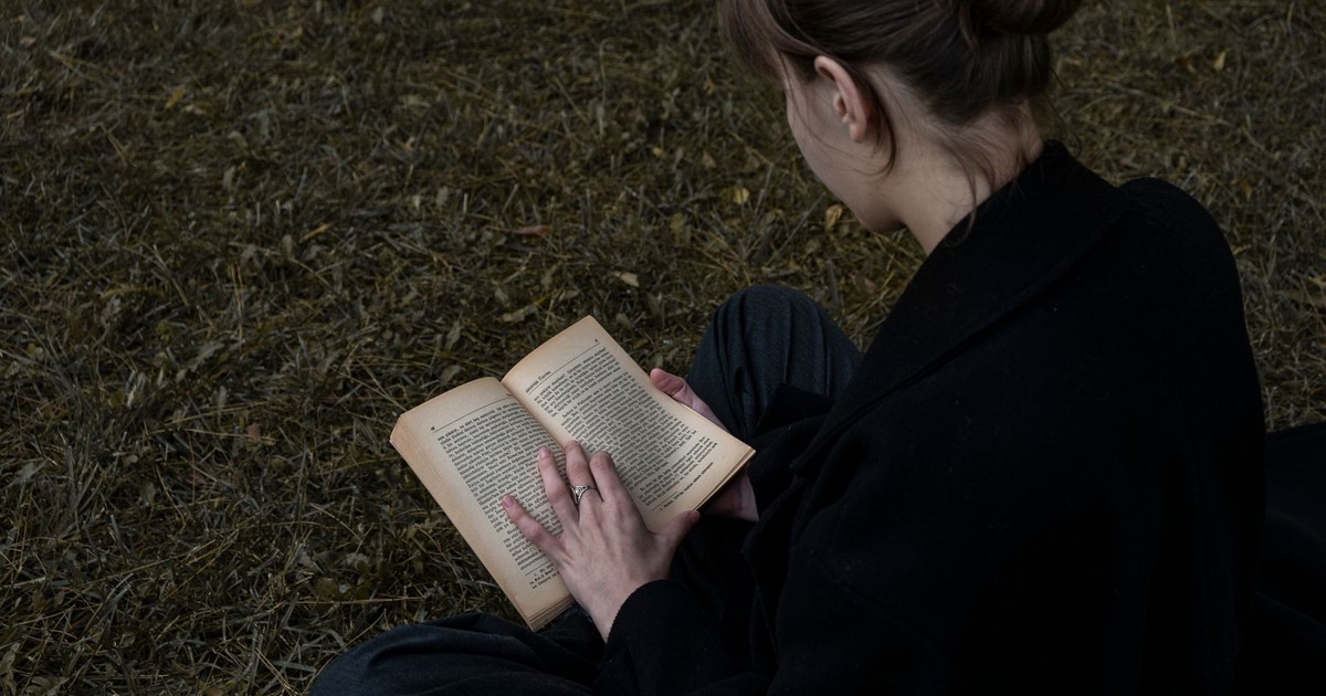 A young woman sits in an outdoor area reading a book, showcasing a peaceful moment of literature in nature.