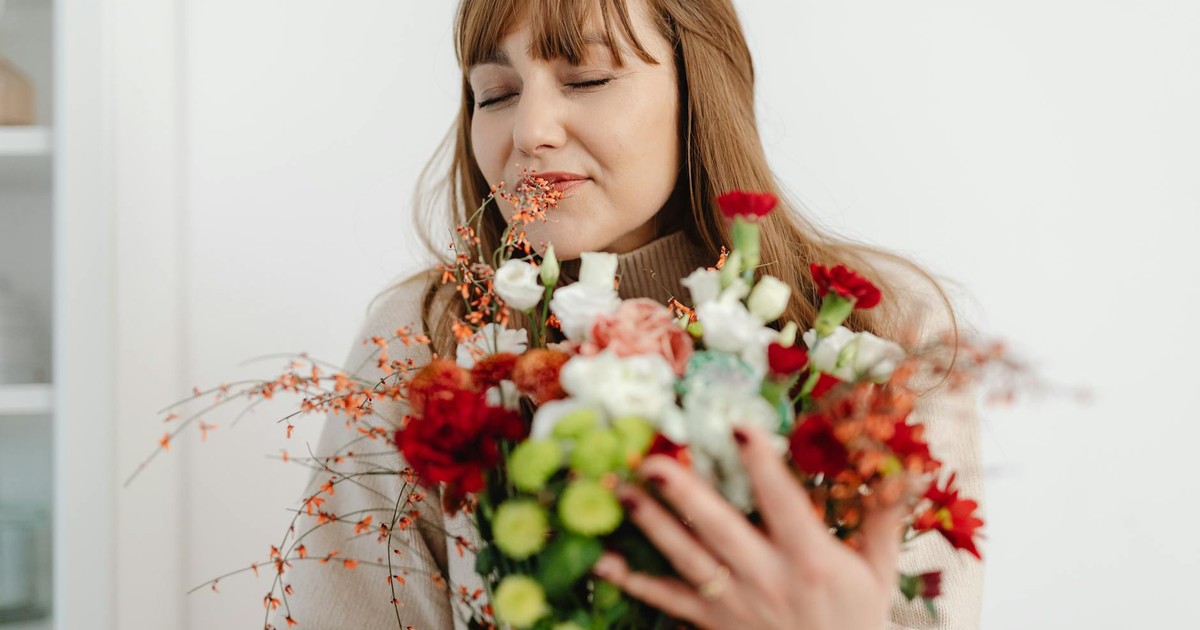 A woman blissfully smelling a colorful bouquet of fresh flowers indoors.