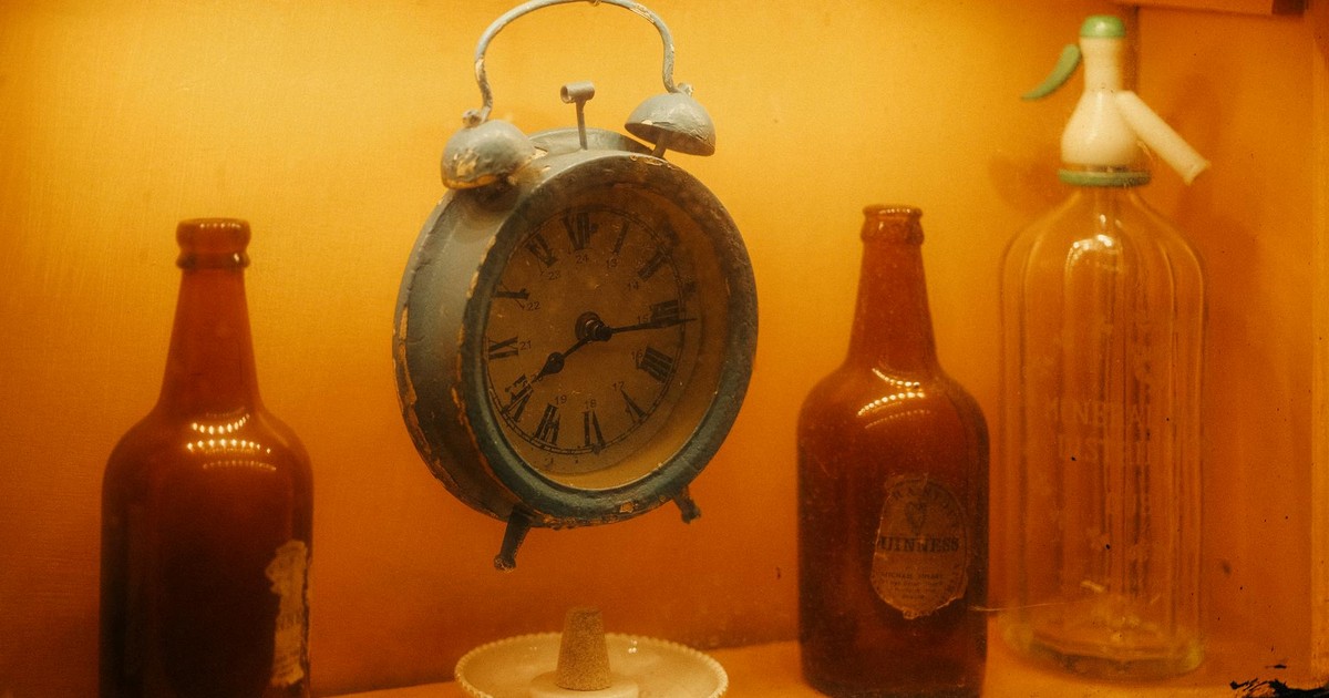 A warm, vintage display featuring a rustic alarm clock surrounded by antique bottles.