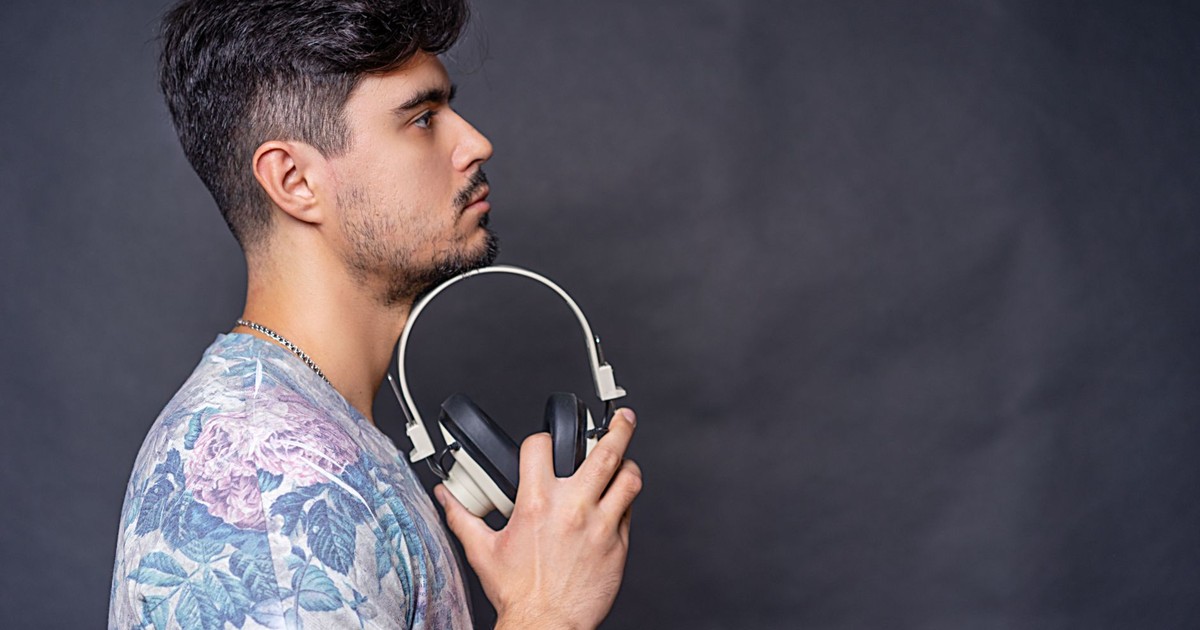 Side view portrait of a man holding headphones in a studio setting against a dark background.