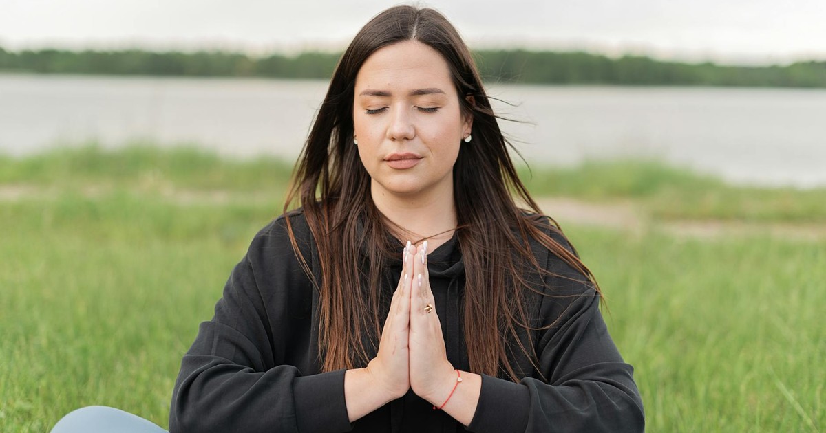 A serene woman practicing meditation outdoors near a lake, promoting wellness and relaxation.