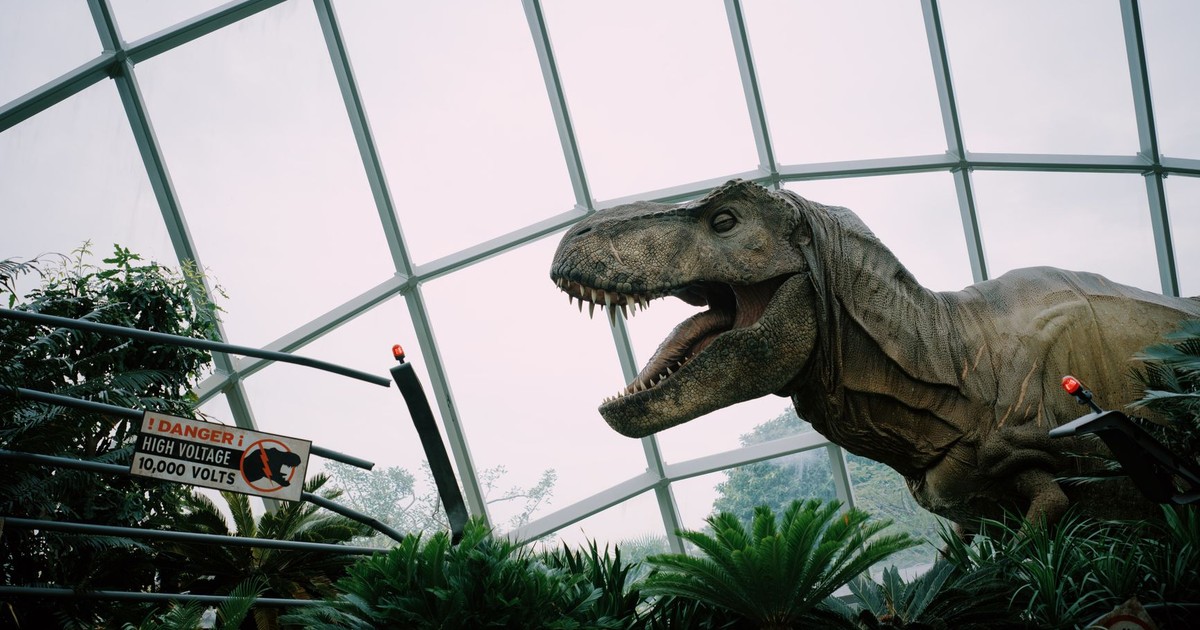 Animatronic T-Rex display in Singapore dome with caution sign amidst lush greenery.