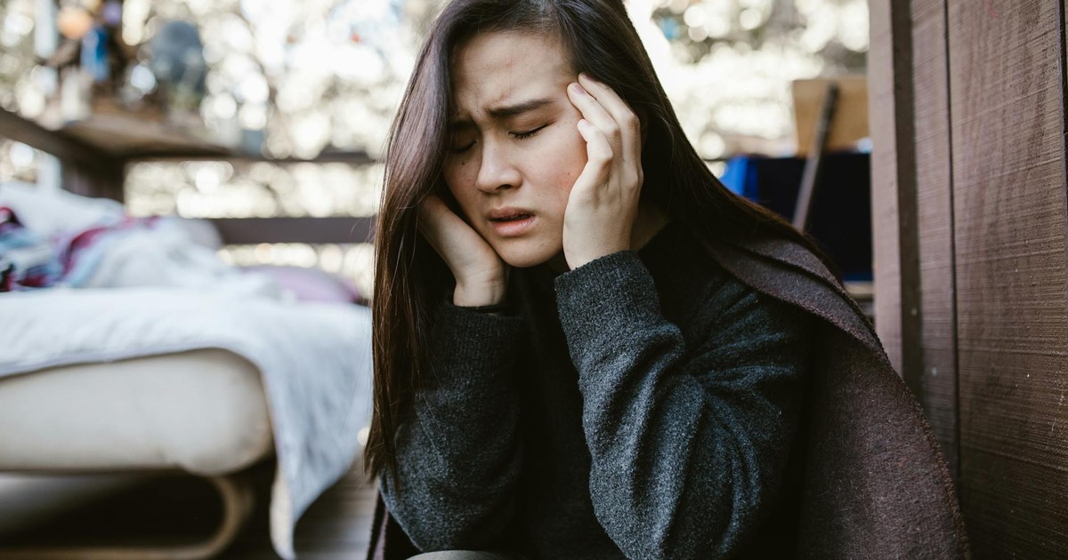 A young woman holds her head in distress while sitting indoors, capturing an emotional moment.