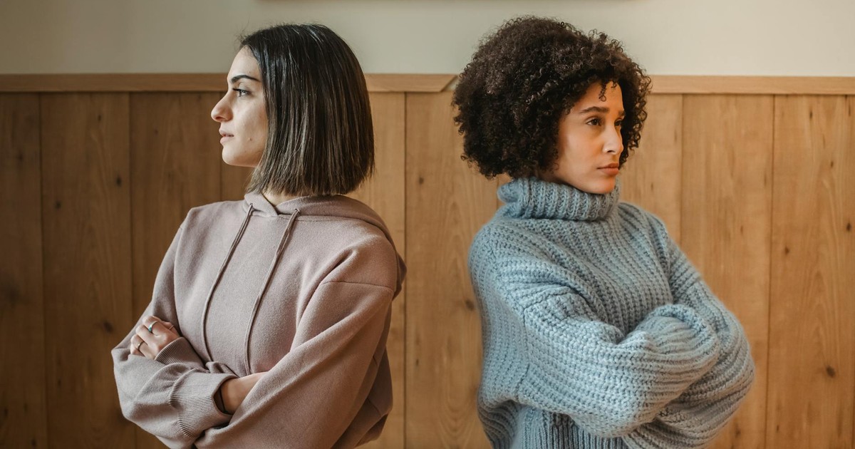 Confident young multiracial ladies in casual clothes standing back to back in light apartment near wall while looking away