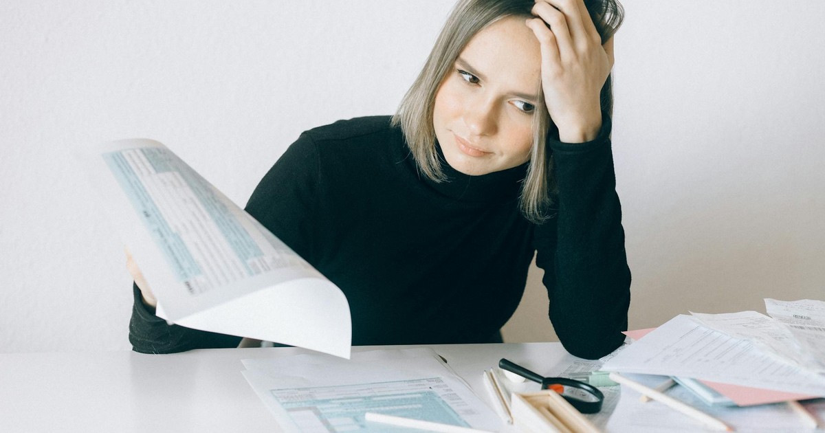 A woman showing stress while reviewing multiple paperwork and financial documents at a desk.