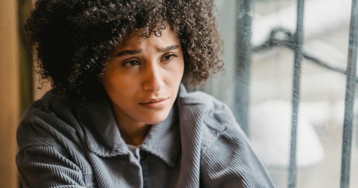 High angle of crop African American female in despair with frown face suffering from trouble sitting near window