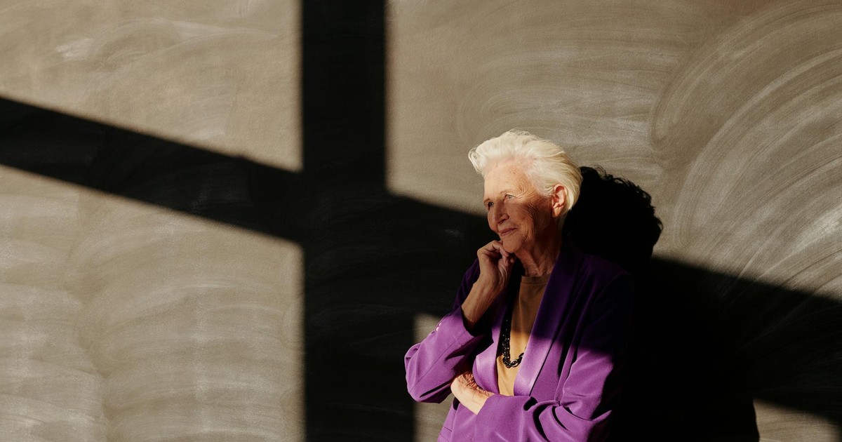 Sophisticated senior woman posing in a purple blazer with striking shadow play on the wall.