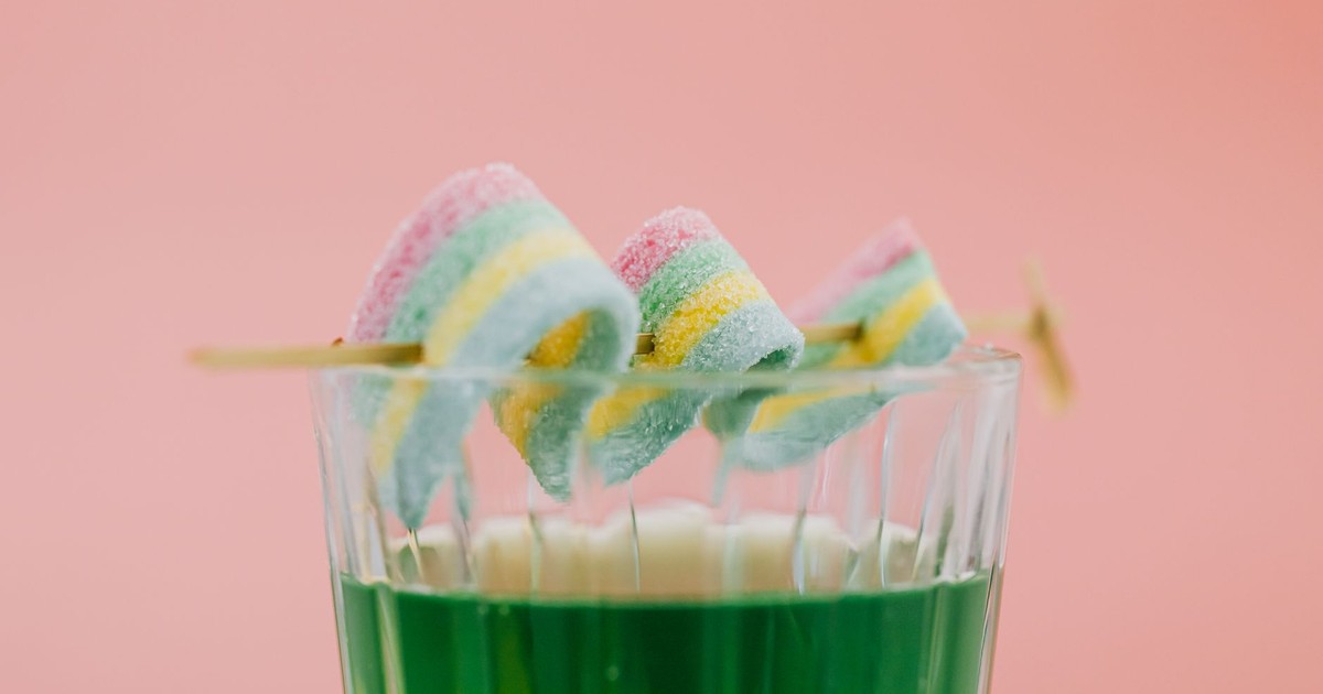 Colorful candy skewers dipped in green beverage against pink backdrop.