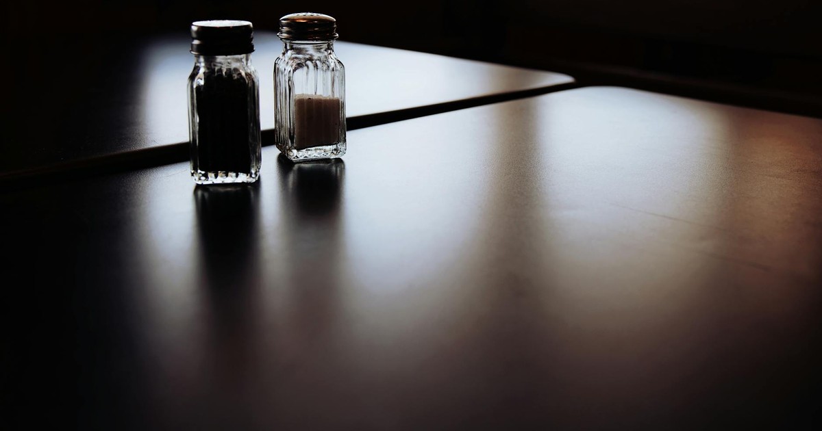 A moody still life of salt and pepper shakers on a dimly lit table.