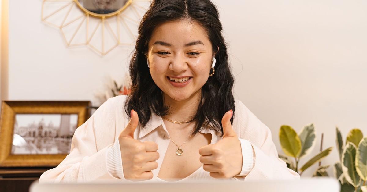 Asian businesswoman giving thumbs up during a successful online meeting, smiling and engaged.
