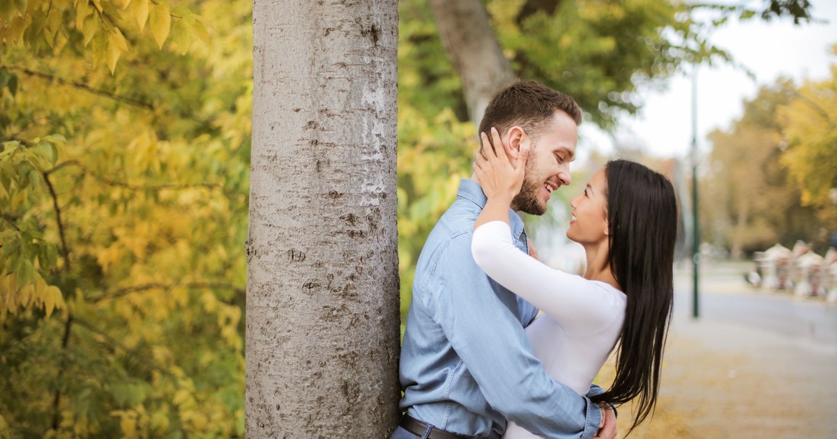 A happy couple embracing by a tree in a scenic autumn park setting.