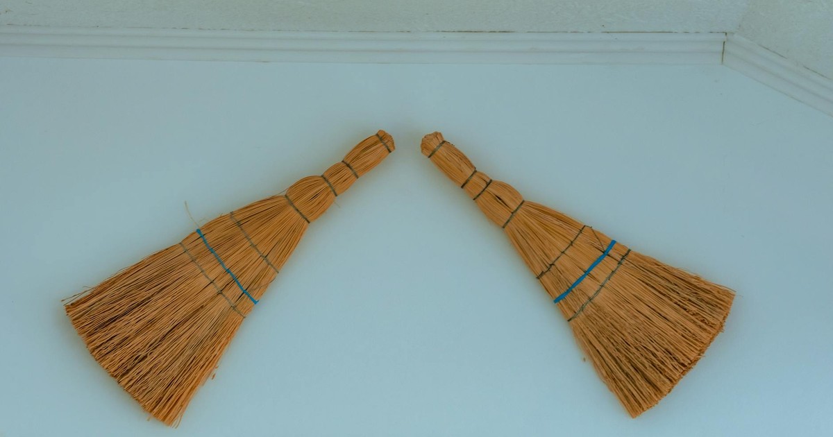 Two decorative rustic straw brooms hanging on a light colored wall.
