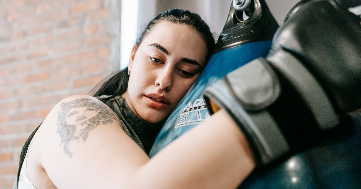 Low angle side view of exhausted young female in boxing gloves having pause in hard training in fitness center