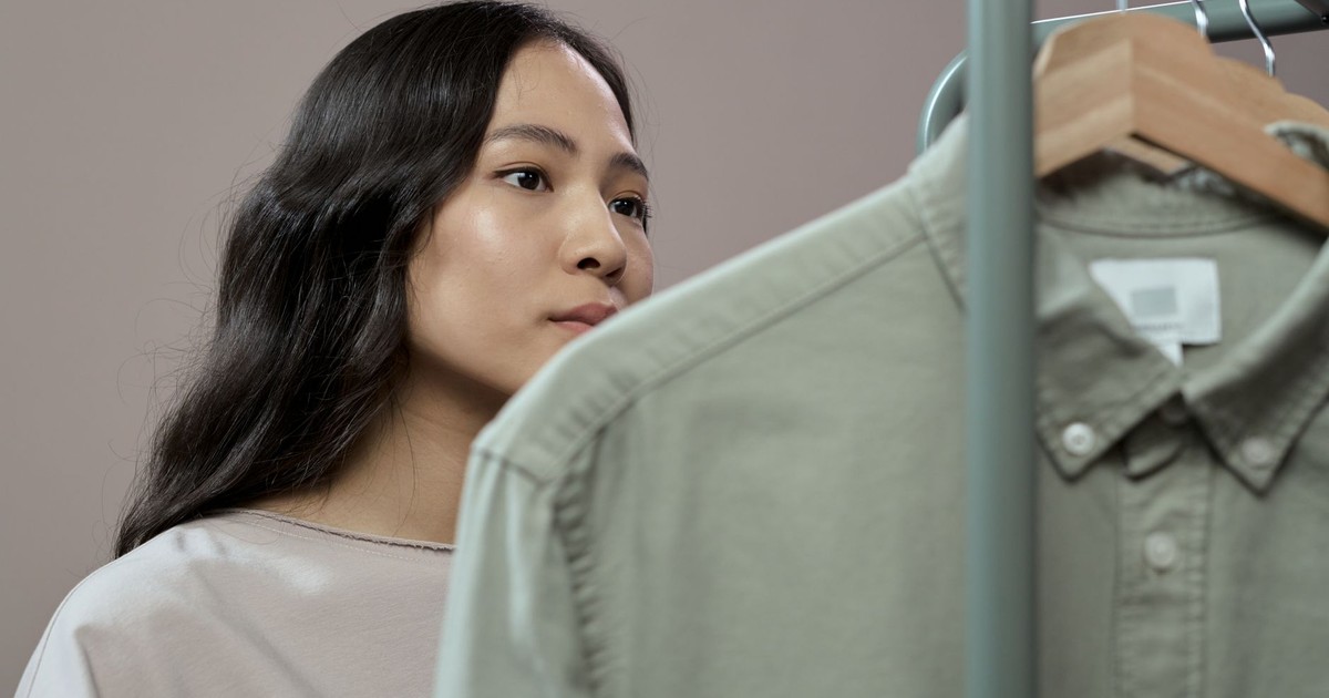 Asian woman thoughtfully browsing clothes in fashion studio, focusing on details.