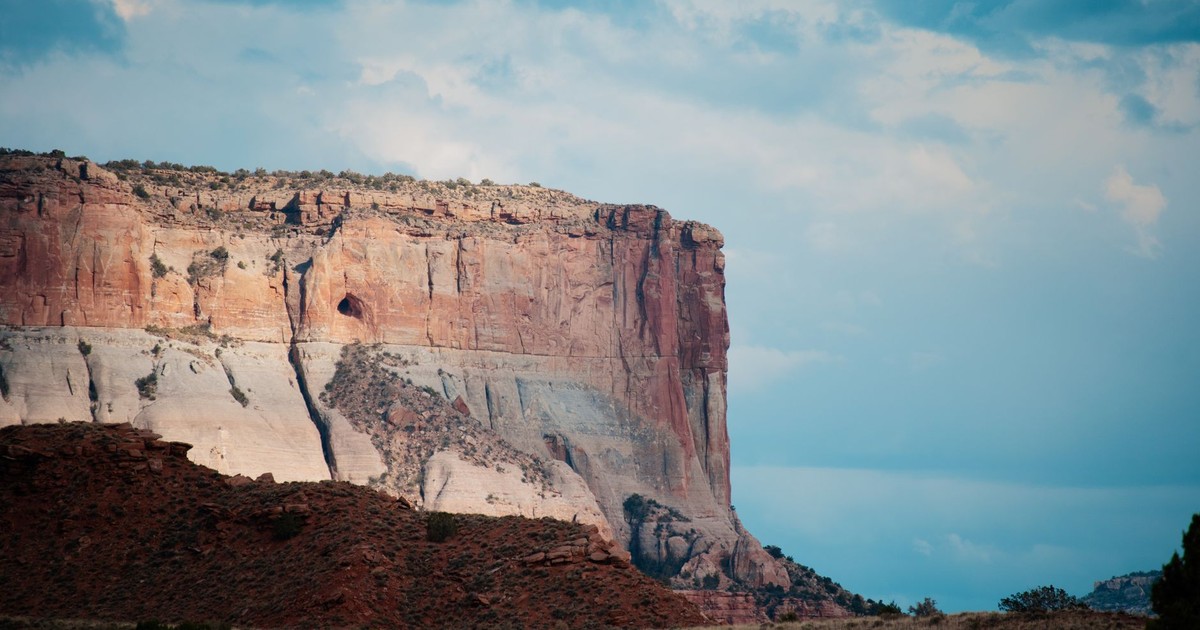 Dramatic shot of a red rock cliff under a cloudy sky in Zuni, showcasing natural beauty and geological formations.