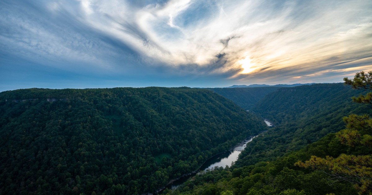 A breathtaking view of a river winding through lush green hills beneath a dramatic sky at sunset.