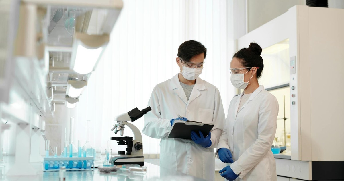 Two scientists in a laboratory wearing masks, discussing research with a microscope.