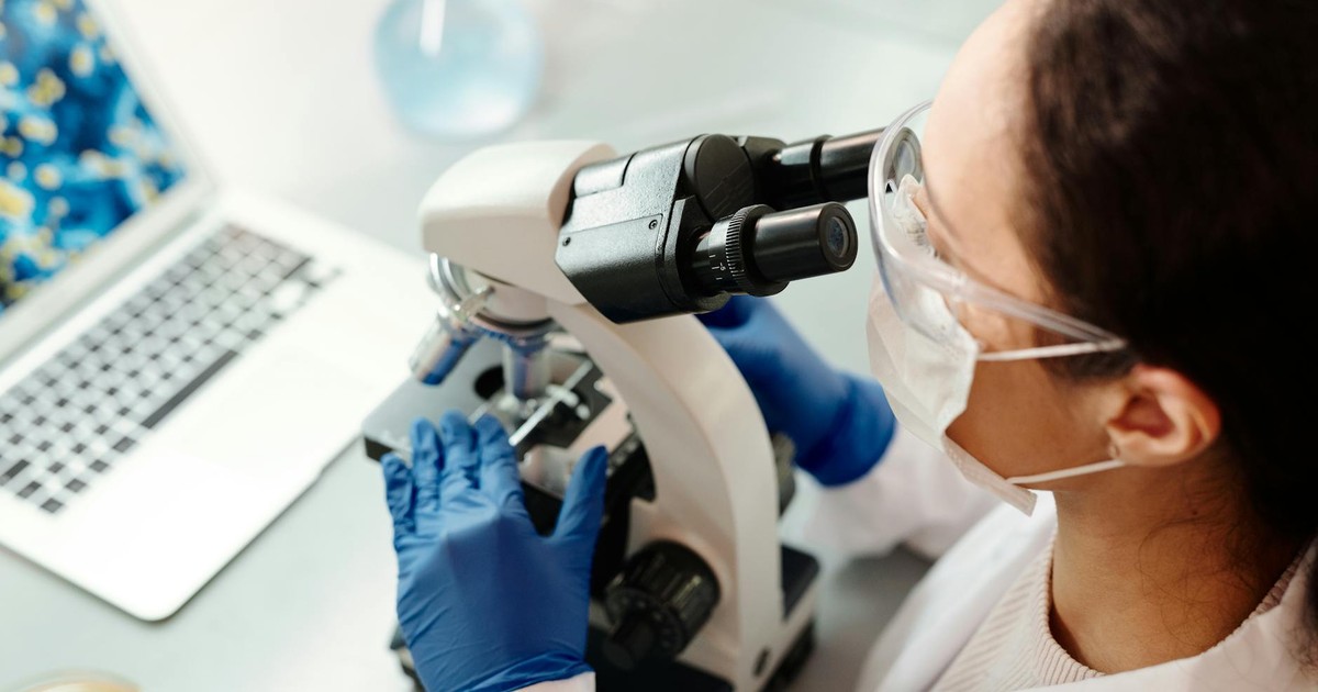 Scientist in protective gear examining samples with microscope in laboratory setting.