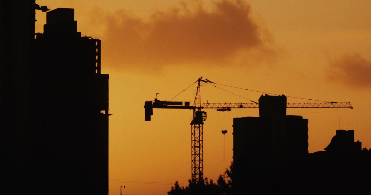 Silhouette of cranes and buildings against a vibrant sunset sky.