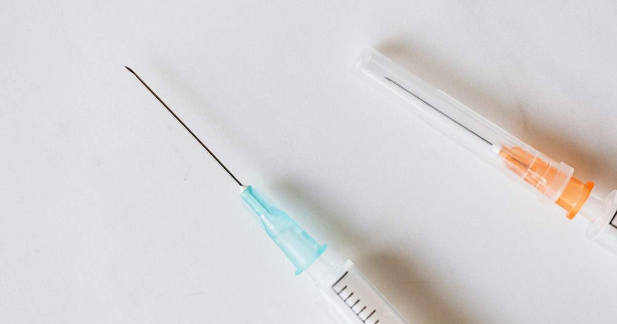 From above of medical syringe with needle placed near syringe with covered needle on white table